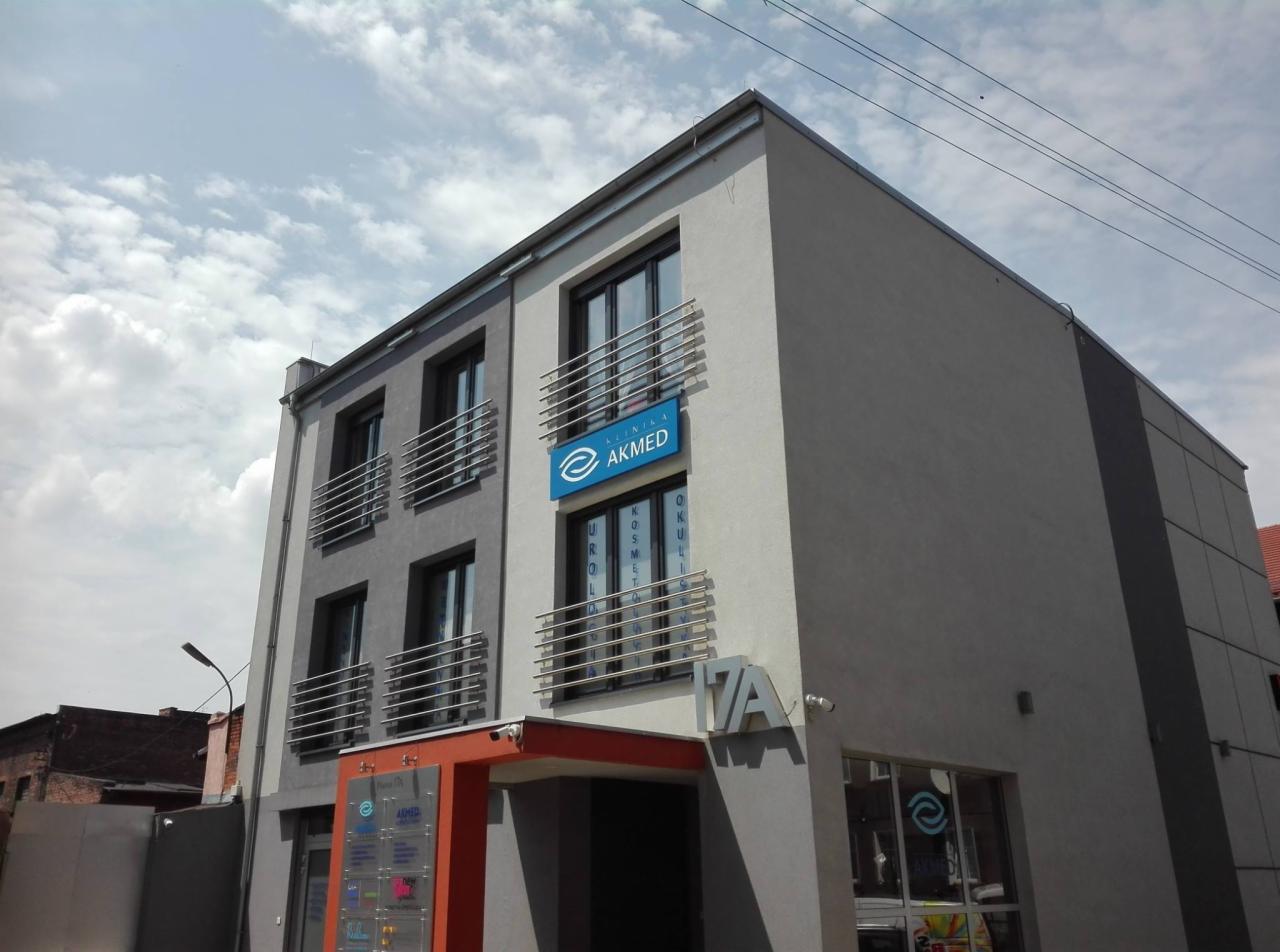 Elewacja budynku kliniki AKMED z niebieskim szyldem z nazwą i logo, widok z zewnątrz w słoneczny dzień.