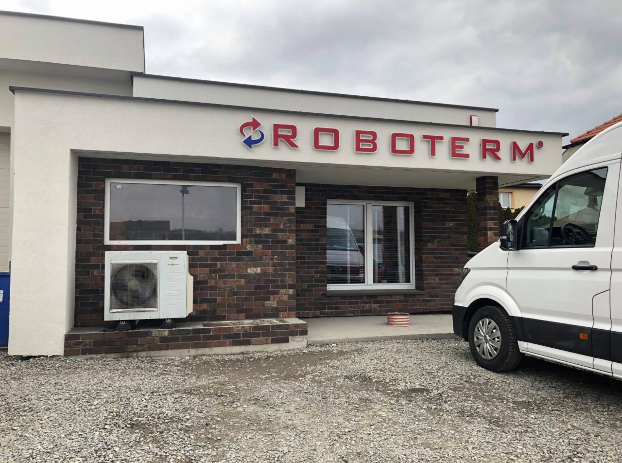 Fasada budynku firmy Roboterm z widocznym logo nad wejściem, klimatyzator na ścianie i zaparkowany biały bus.