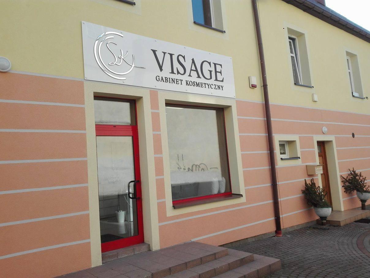 Zewnętrzny widok budynku gabinetu kosmetycznego z szyldem z logo i nazwą 'VISAGE' nad wejściem.
