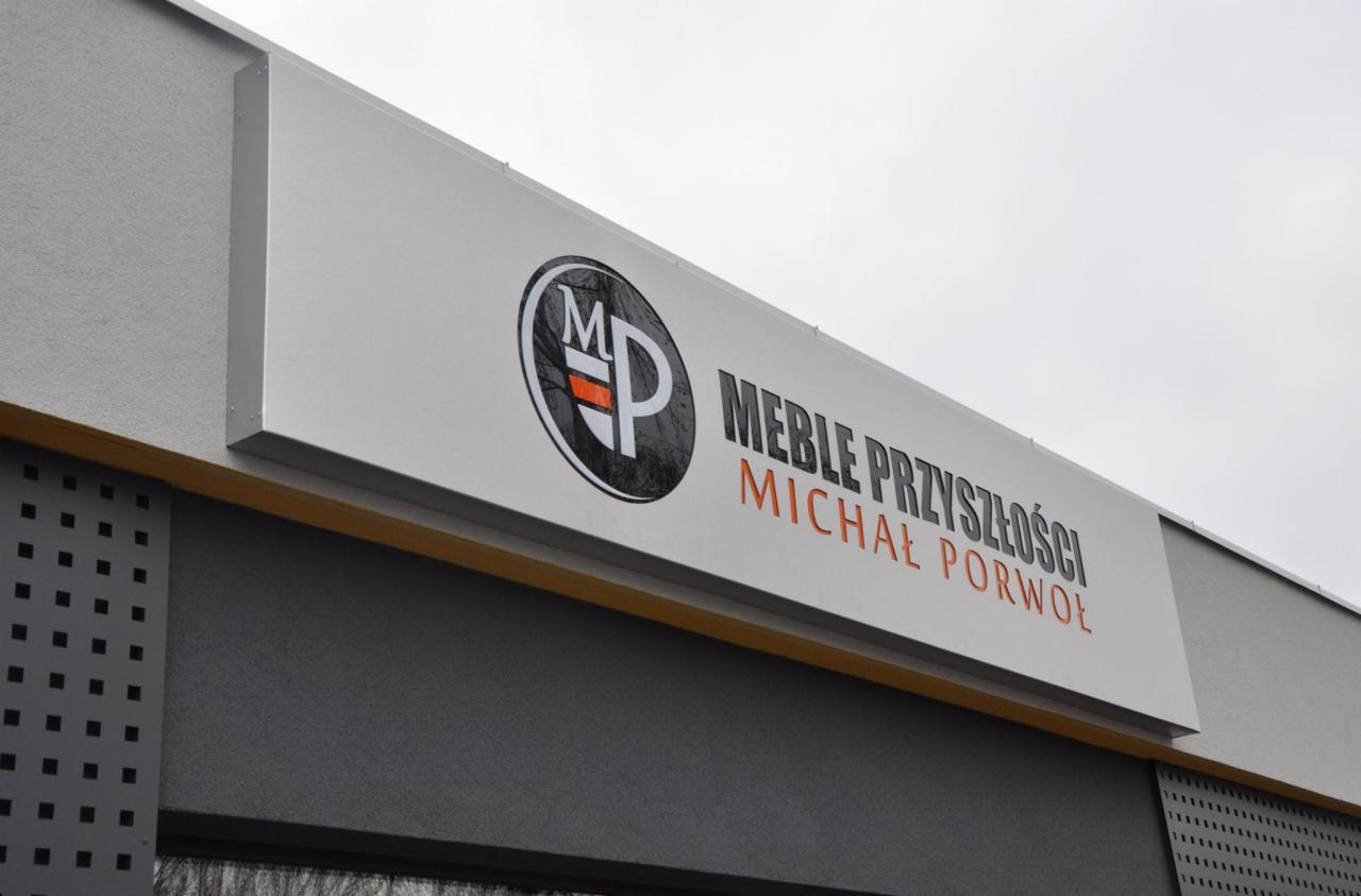 Szyld reklamowy firmy Meble Przyszłości Michał Porwoł z logo MP na elewacji budynku, widok z dołu.