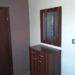 Przedpokój po remoncie: brązowe panele podłogowe, szafka z lustrem w drewnianej ramie, ściany w kolorze złamanej bieli i brązu.