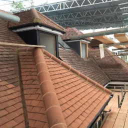 Montaż okien dachowych w skośnym dachu pokrytym czerwoną dachówką, widok z rusztowania.