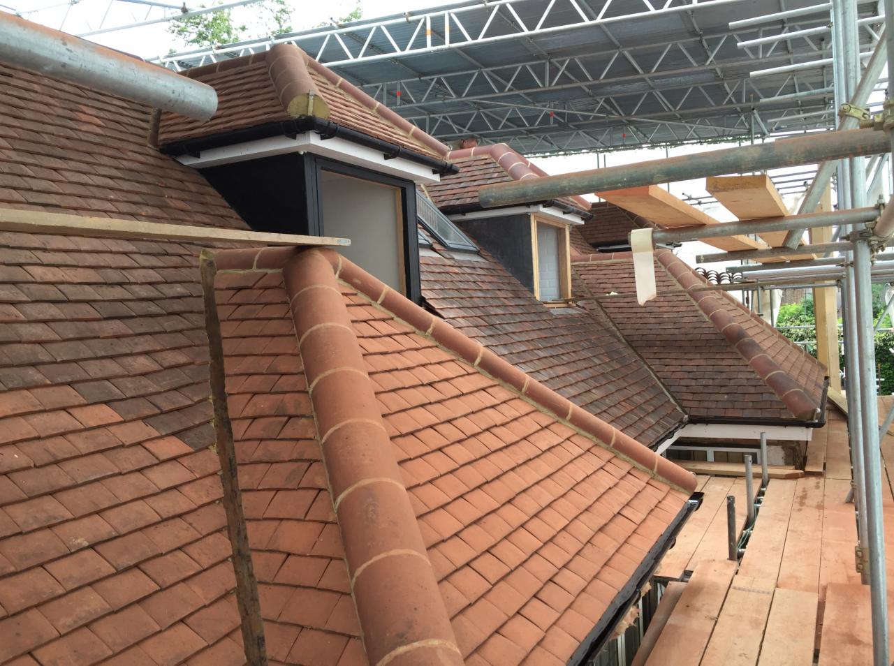 Montaż okien dachowych w skośnym dachu pokrytym czerwoną dachówką, widok z rusztowania.