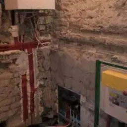 Montaż ogrzewania podłogowego z widocznym kotłem gazowym na tle surowej, kamiennej ściany.