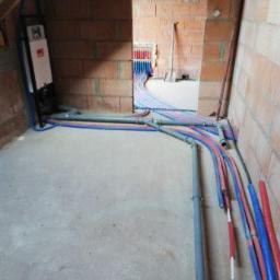 Mti - Surowy stan wnętrza z widocznymi instalacjami wodno-kanalizacyjnymi w rurach niebieskich i czerwonych, oraz szarymi rurami kanalizacyjnymi, ściany z czerwonej cegły, widoczny rozdzielacz na ścianie.