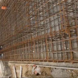 Siatka zbrojeniowa przygotowana do zalania betonem, widoczni pracownicy w odblaskowych kamizelkach na budowie.