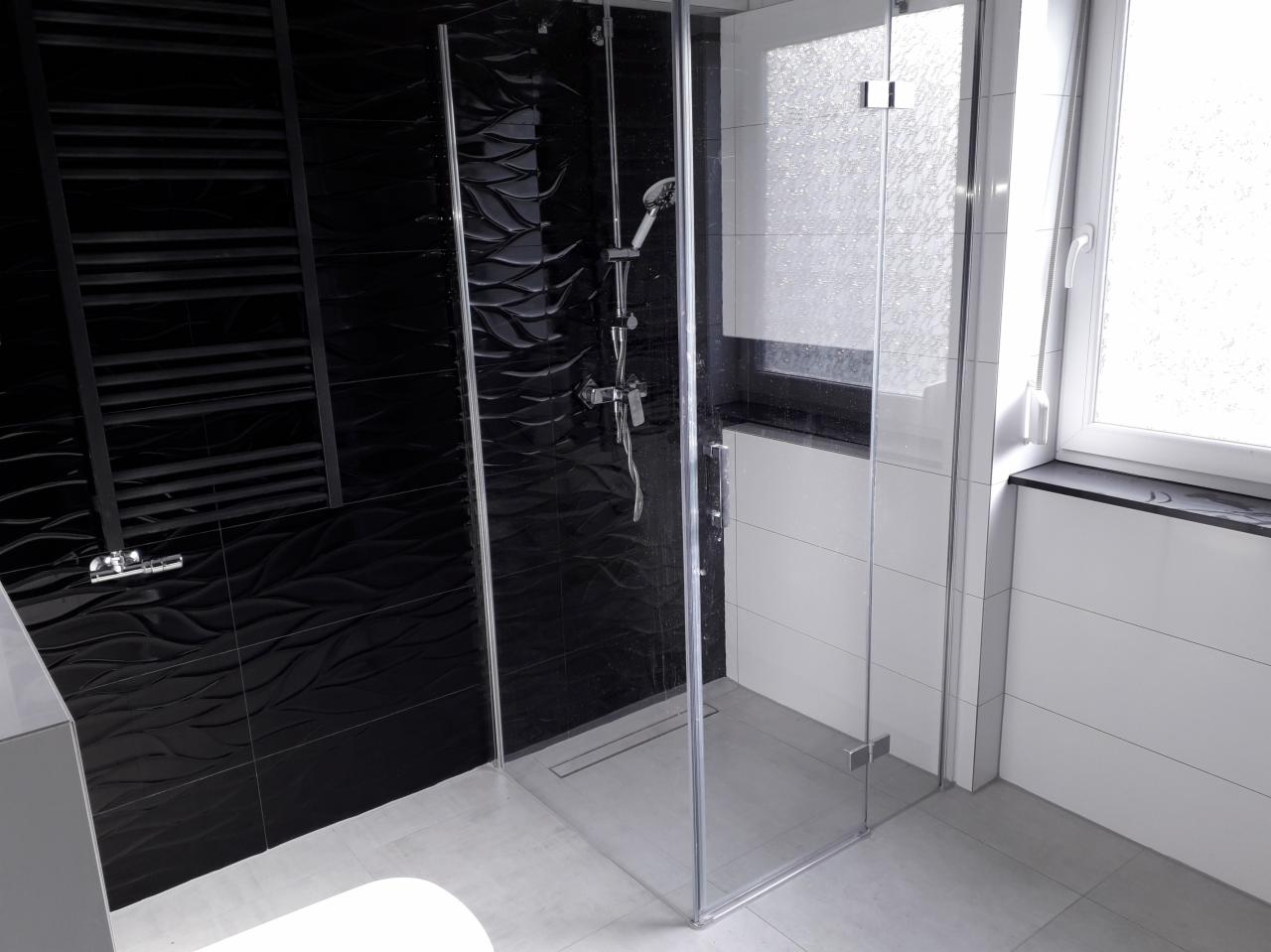 Nowoczesna kabina prysznicowa z czarnymi płytkami o falistej strukturze i grzejnikiem drabinkowym, kontrastująca z białymi płytkami i oknem.