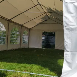 Wnętrze białego namiotu imprezowego z oknami na trawniku, widok na zewnątrz przez wejście, metalowa konstrukcja dachu.