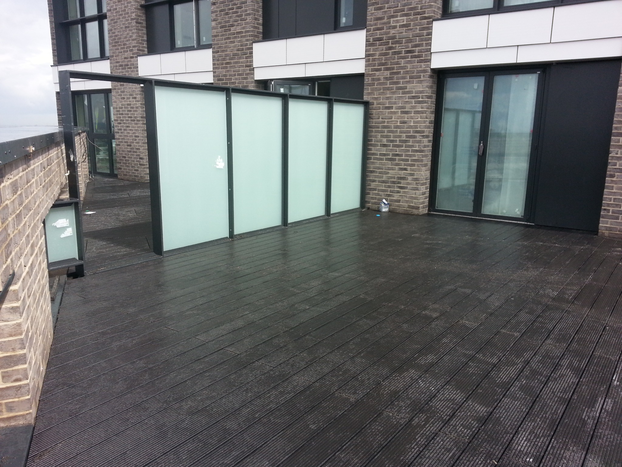 Ciemny taras kompozytowy na balkonie nowoczesnego apartamentowca z przesłonami z matowego szkła, widok na horyzont w pochmurny dzień.