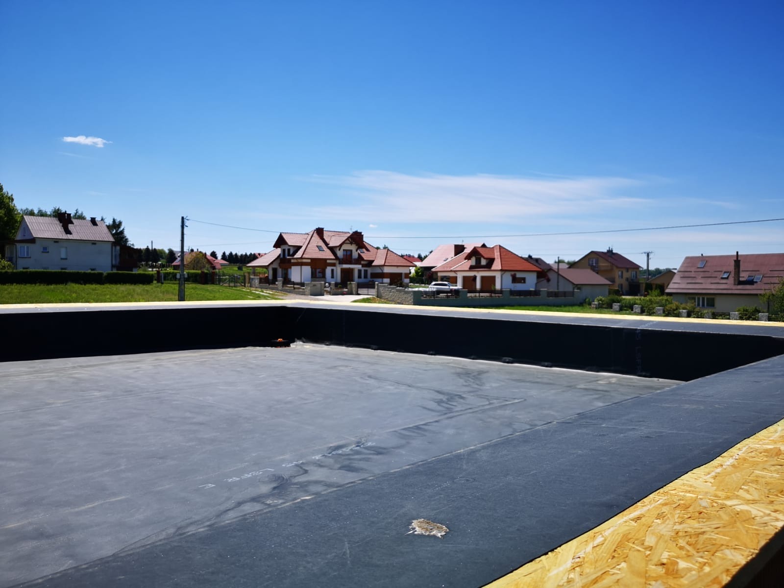Czarna membrana dachowa ułożona na nowej konstrukcji dachu, widoczne okoliczne domy i błękitne niebo.