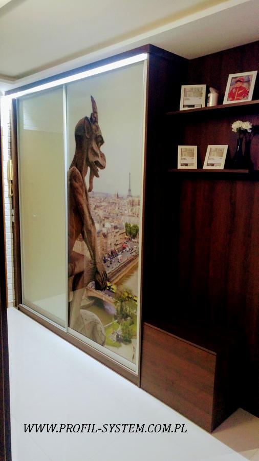 Szafa przesuwna z grafiką przedstawiającą gargulca na tle panoramy Paryża, widoczna część wnętrza i półki boczne w kolorze ciemnego drewna.