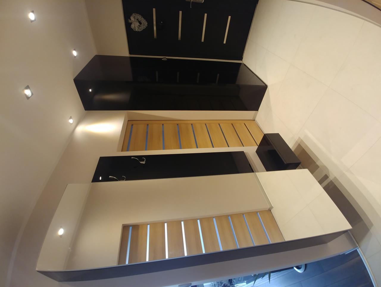 Nowoczesny przedpokój z zabudową w kolorach czerni, bieli i drewna, z oświetleniem punktowym i wieszakami na ścianie.