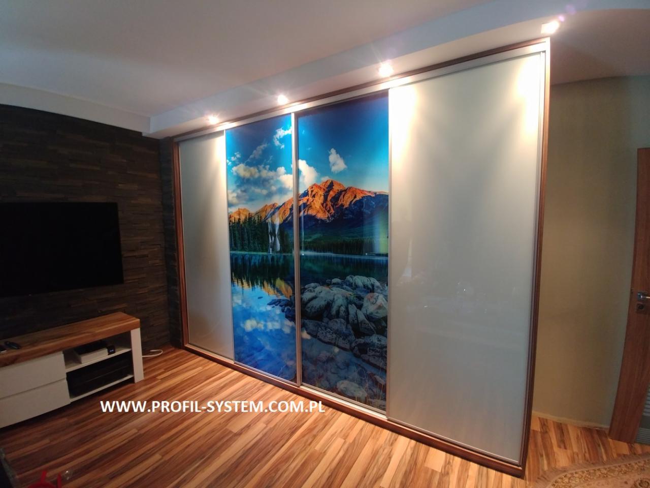 Szafa wnękowa z przesuwnymi drzwiami z grafiką górskiego krajobrazu, widoczna w salonie z drewnianą podłogą i panelem ściennym imitującym kamień.