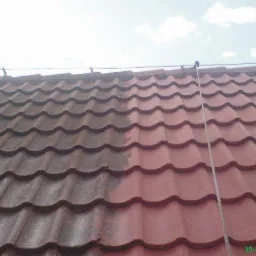 Częściowo umyty dach z czerwonej dachówki, widoczna różnica w kolorze między czystą a zabrudzoną powierzchnią, lanca do mycia na dachu.