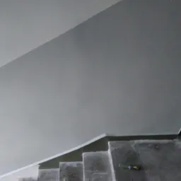 Szare poddasze po ociepleniu, widoczne fragmenty schod&oacute;w i narzędzie na jednym ze stopni.