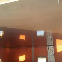 Świeżo wylana, gładka wylewka betonowa w surowym wnętrzu budynku z czerwonej cegły, z widoczną drabiną i refleksami światła słonecznego w oknach.