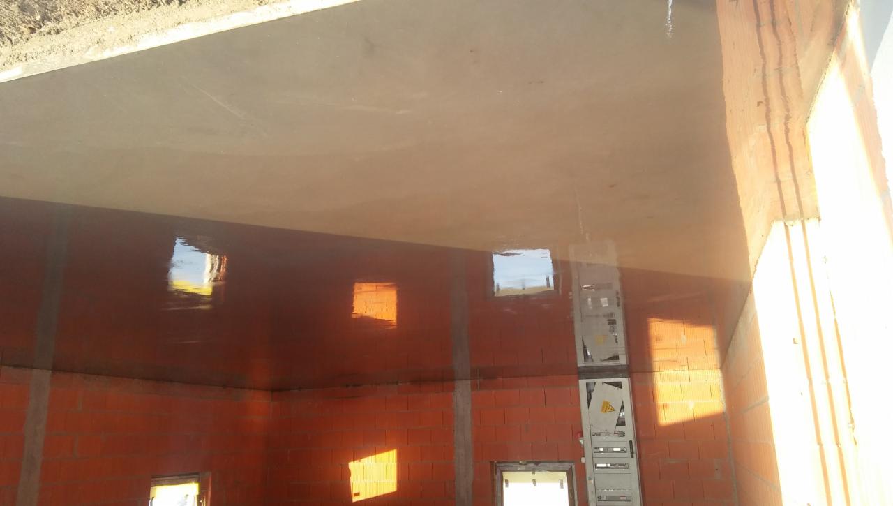 Świeżo wylana, gładka wylewka betonowa w surowym wnętrzu budynku z czerwonej cegły, z widoczną drabiną i refleksami światła słonecznego w oknach.