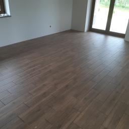 ADIBAU - Ułożona podłoga z płytek imitujących drewno w salonie w Wodzisławiu Śląskim. Widoczne okno balkonowe i przygotowane ściany do malowania.