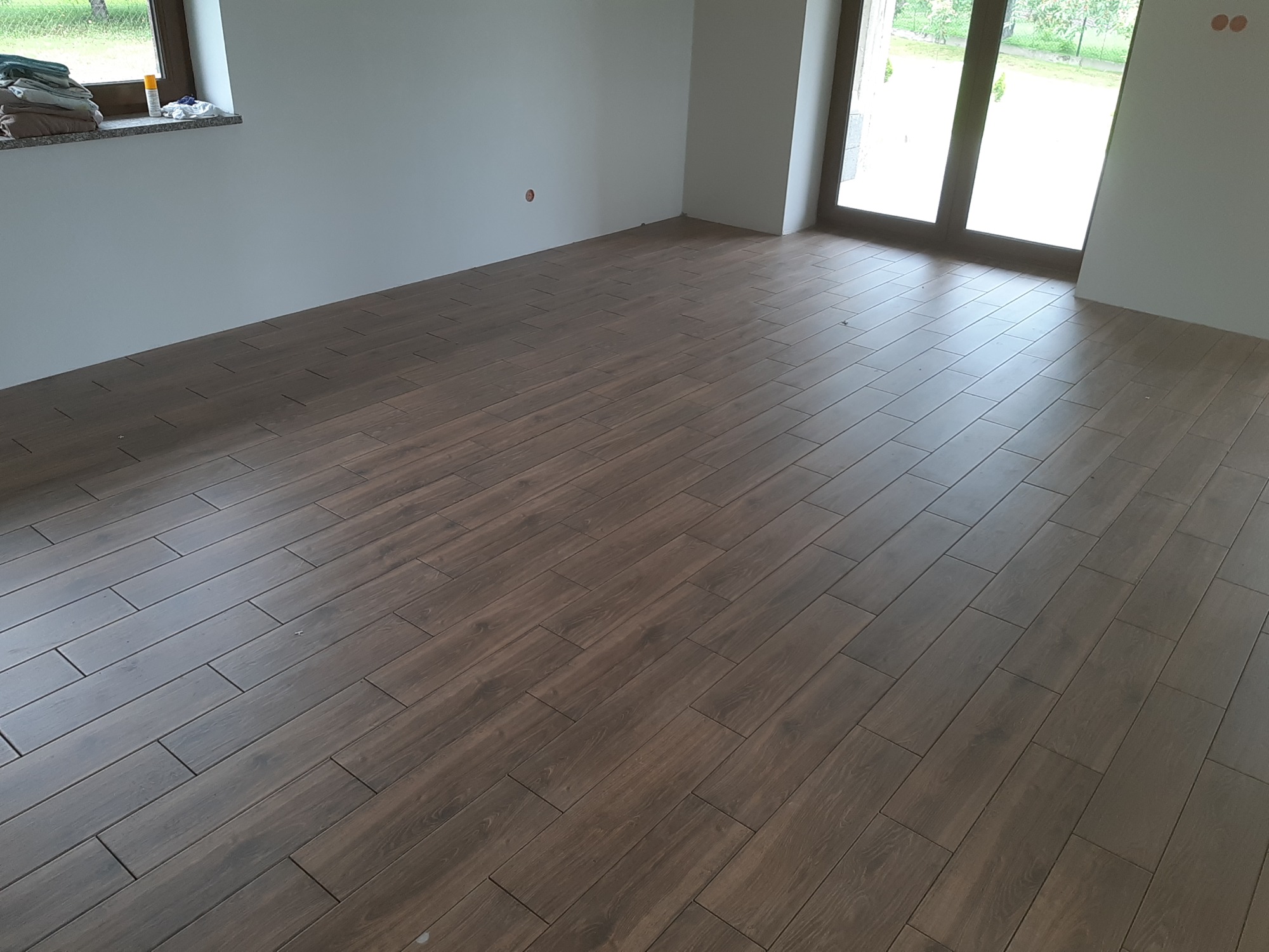 Ułożona podłoga z płytek imitujących drewno w salonie w Wodzisławiu Śląskim. Widoczne okno balkonowe i przygotowane ściany do malowania.