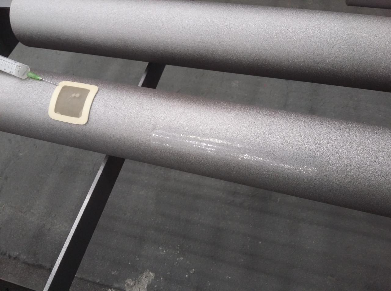 Szary, metalowy element konstrukcyjny w trakcie testowania nieniszczącego z użyciem strzykawki i elektrody.