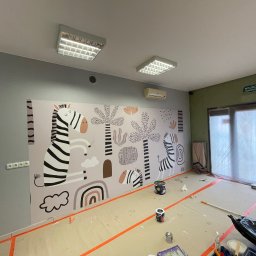 Zakład ogólnobudowlany Damian Pawlak - Pokój w trakcie malowania z motywem zebry i roślin na ścianie, widoczne puszki z farbą i taśma malarska na podłodze zabezpieczonej folią.