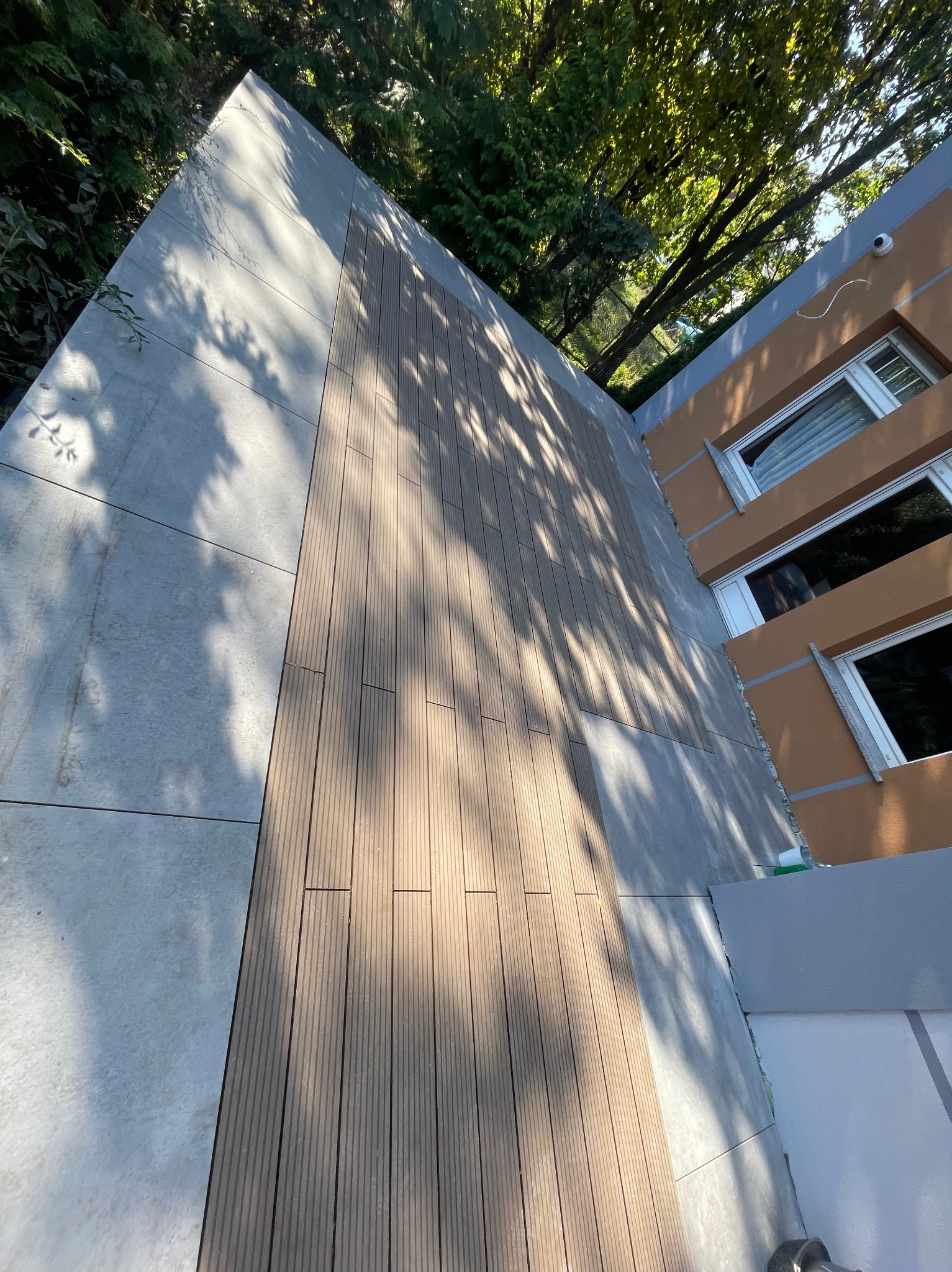 Wykończona elewacja budynku z elementami drewnopodobnymi i płytami kamiennymi, widok z dołu na fragment elewacji i drzewa.