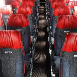 Wnętrze autobusu z rzędami czerwono-szarych foteli Van Hool, widok wzdłuż korytarza, czerwone zasłony na przedniej szybie.