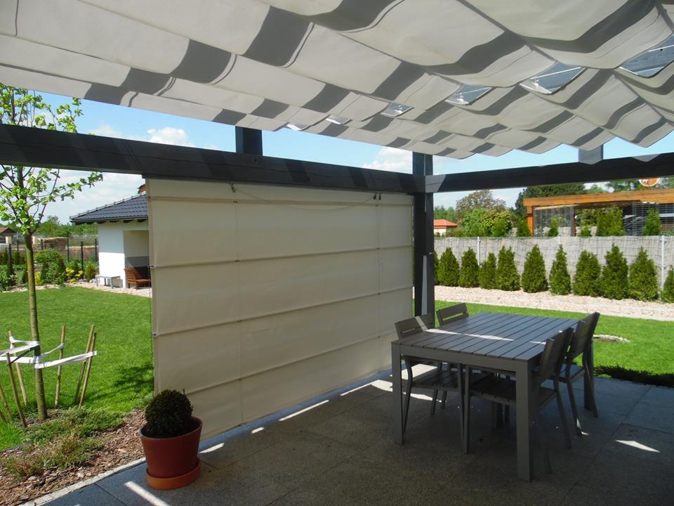 Nowoczesna pergola z tkaninowym zadaszeniem w biało-szare pasy, osłonięty taras z szarą podłogą i stołem z krzesłami, widok na zadbany trawnik i ogród.