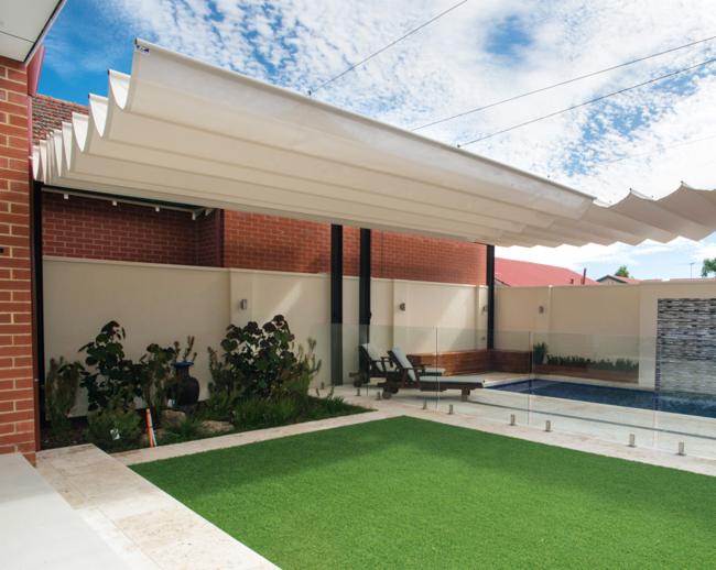 Nowoczesny ogród z basenem i zadaszeniem z falistą tkaniną, widok na zielony trawnik, jasne ściany i szklane balustrady.