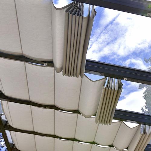 Zasuwana, beżowa markiza materiałowa zamontowana na metalowej konstrukcji, widok z dołu na tle błękitnego nieba z chmurami.