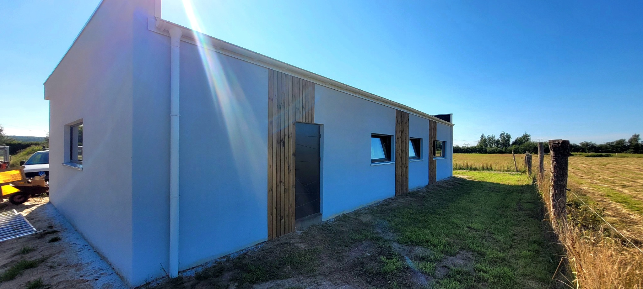 Nowoczesny dom szkieletowy z białymi ścianami i drewnianymi akcentami, widok z zewnątrz w słoneczny dzień. Widoczne okna i drzwi z ciemnymi ramami.