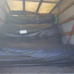 Wnętrze przestrzeni ładunkowej z rolowanymi materiałami zabezpieczonymi czarną folią, widoczne pasy transportowe.