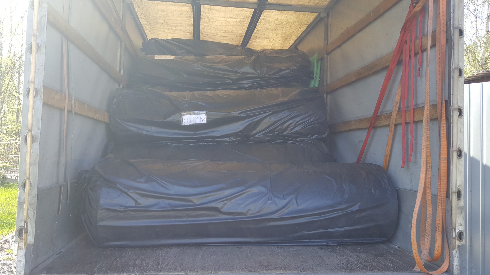 Wnętrze przestrzeni ładunkowej z rolowanymi materiałami zabezpieczonymi czarną folią, widoczne pasy transportowe.