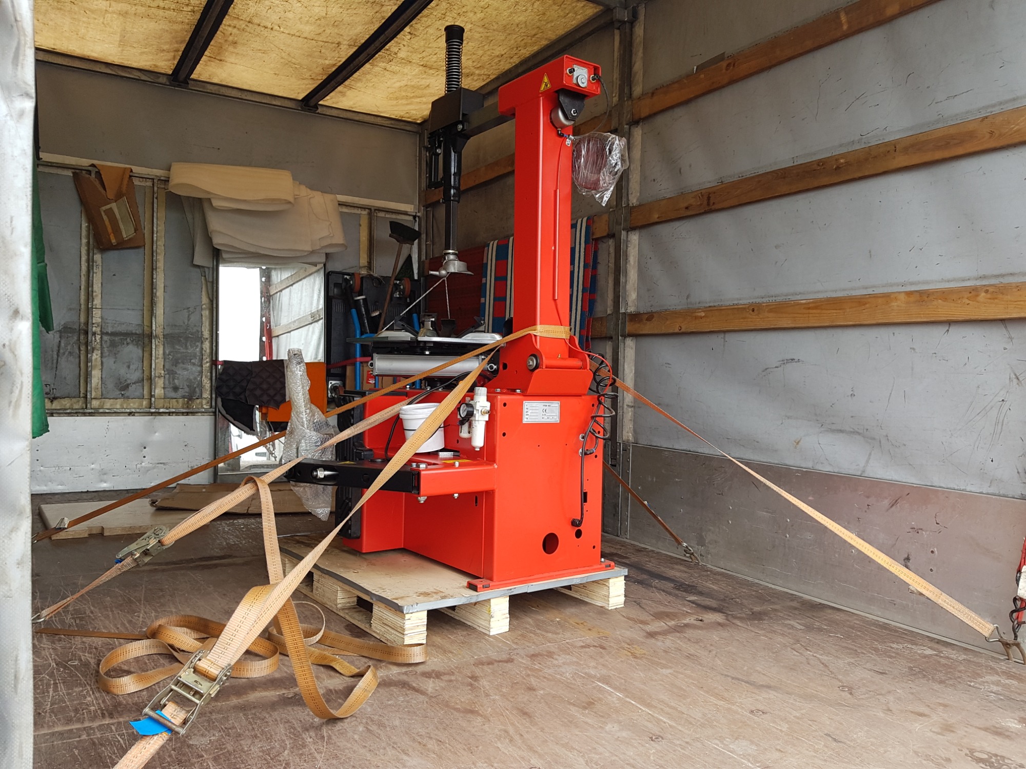 Czerwona montażownica do opon, zabezpieczona pasami transportowymi na palecie wewnątrz przestrzeni ładunkowej pojazdu.