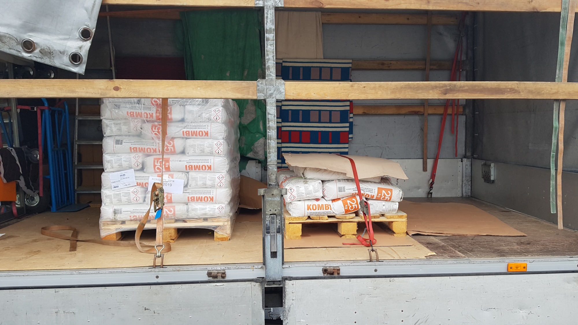 Wnętrze przestrzeni ładunkowej busa z zabezpieczonymi paletami worków z materiałami budowlanymi, widoczne pasy mocujące i zabezpieczające ładunek podczas transportu.