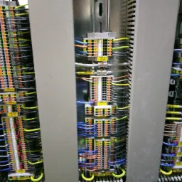 Rozdzielnica elektryczna z widocznymi listwami zaciskowymi, przewodami o różnych kolorach i oznaczeniami, zainstalowana w szarej obudowie.