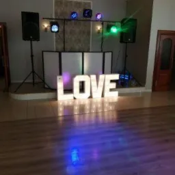 Sala z dekoracją świetlną LOVE, kolumny głośnikowe na statywach i oświetlenie sceniczne, przygotowana na imprezę.