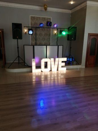 Sala z dekoracją świetlną LOVE, kolumny głośnikowe na statywach i oświetlenie sceniczne, przygotowana na imprezę.