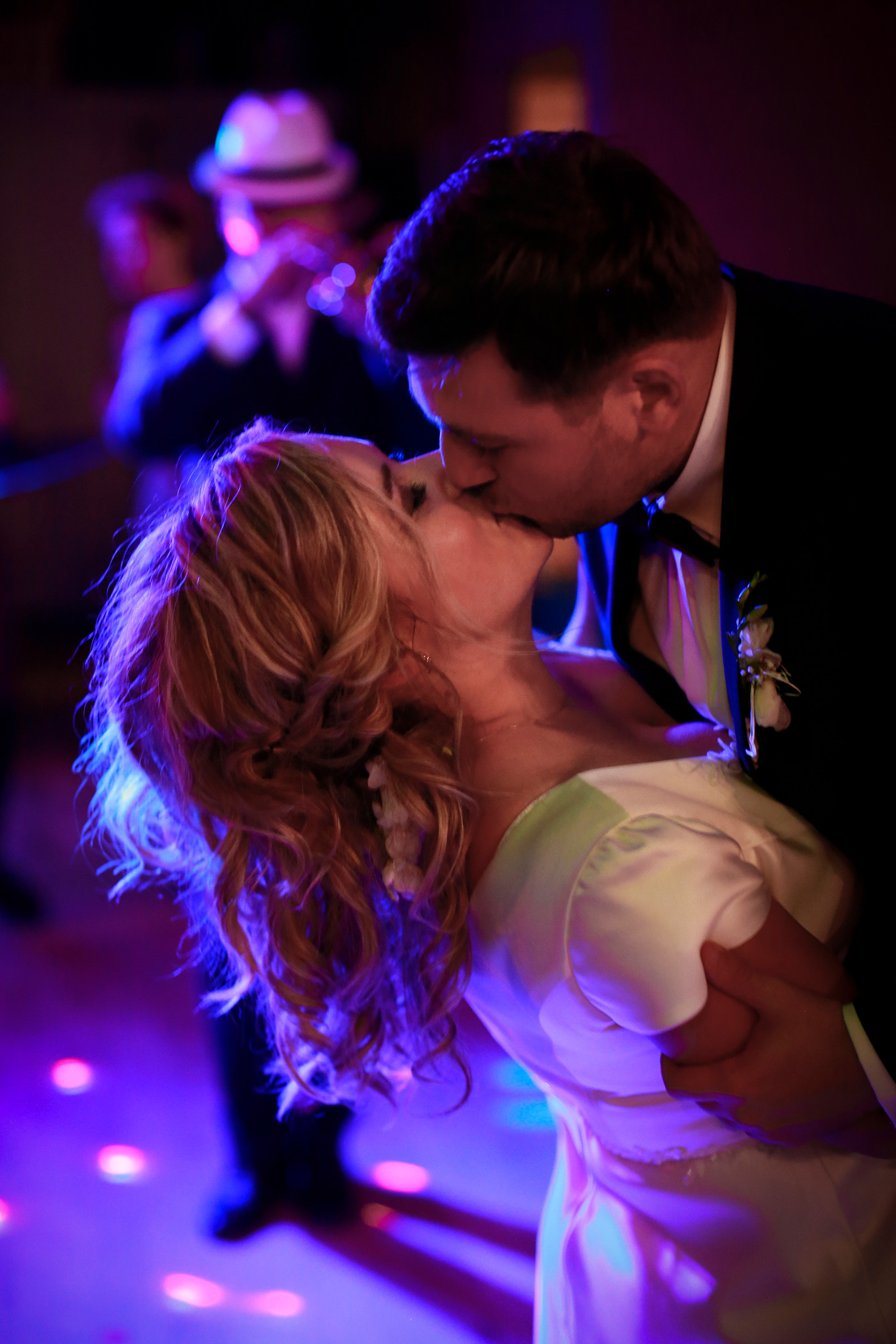 Pocałunek nowożeńców w tańcu, w tle muzyk z trąbką i światła dyskotekowe.