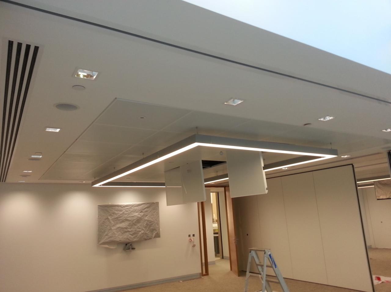 Biuro z podwieszanym sufitem kasetonowym, oświetleniem LED, klimatyzacją i częściowo zasłoniętą ścianą, widoczna drabina.