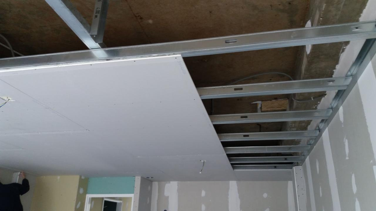 Montaż płyty na metalowym ruszcie sufitowym, widoczne przewody elektryczne, fragment ściany z widocznymi śladami szpachlowania.