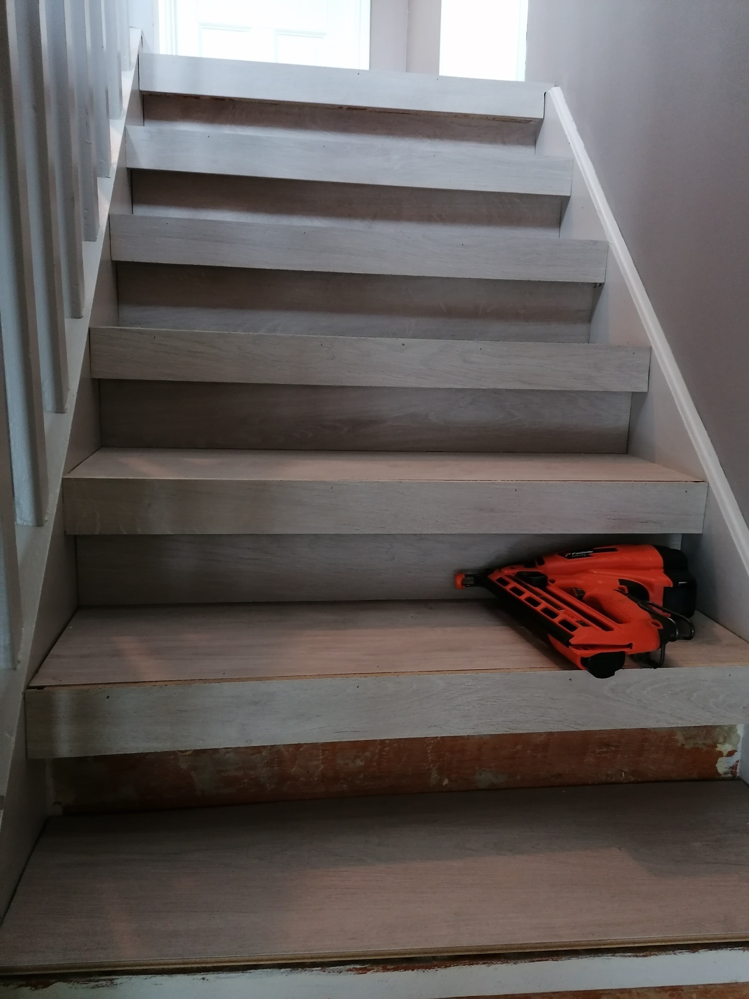 Montaż drewnianych paneli schodowych, widoczny pomarańczowy pistolet do gwoździ na jednym ze stopni.