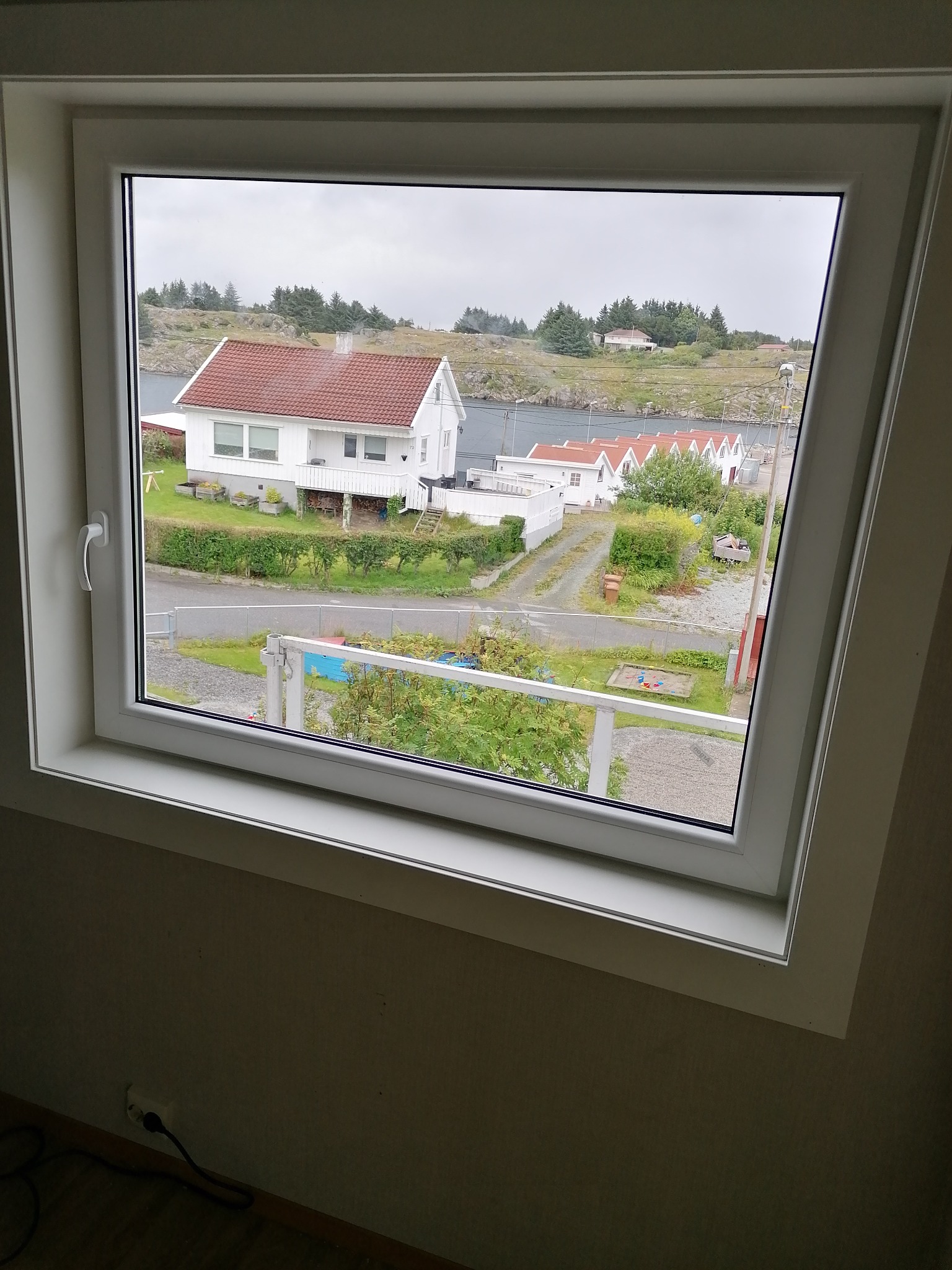 Widok z okna na osiedle domków jednorodzinnych z czerwonymi dachami w nadmorskiej miejscowości, pochmurne niebo.