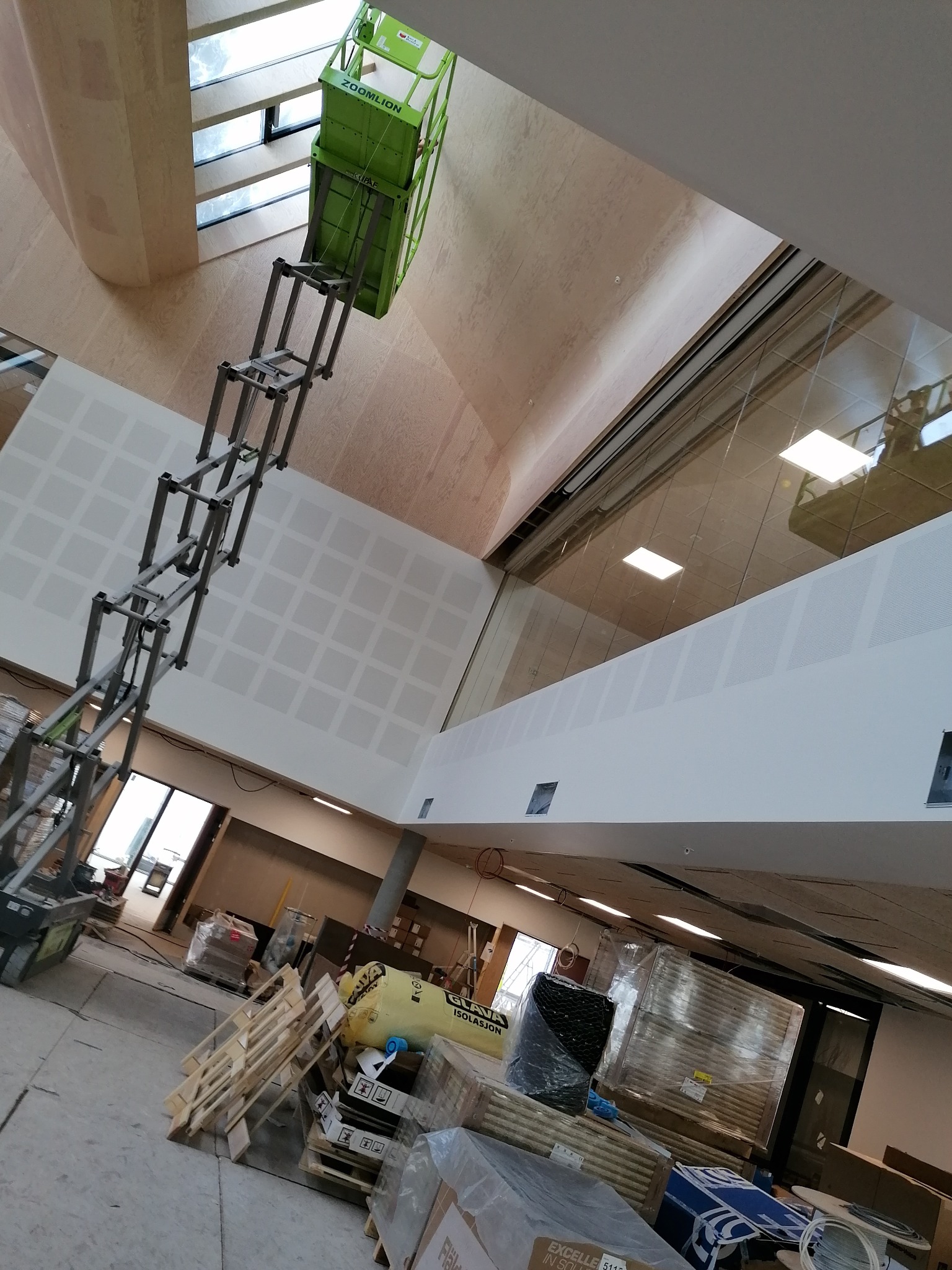 Wysięgnik koszowy Zoomlion ustawiony wewnątrz budynku, widoczna ściana z nałożoną siatką kwadratów, materiały budowlane na podłodze, okna w suficie.