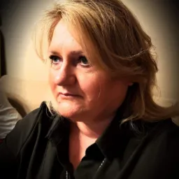 Portret kobiety o blond włosach, w czarnej koszuli, spoglądającej w bok. Zdjęcie wykonane w Warszawie, w stonowanej kolorystyce.