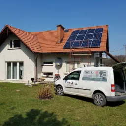 Dom jednorodzinny z panelami słonecznymi na dachu, drabina oparta o dach, biały samochód dostawczy z otwartym bagażnikiem i logo firmy na boku, słoneczny dzień.