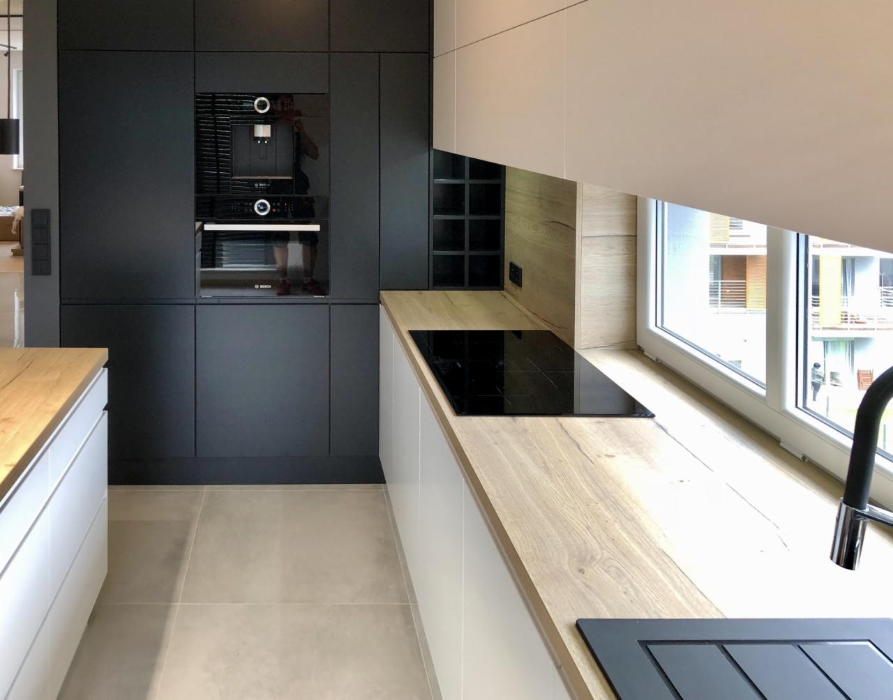 Nowoczesna zabudowa kuchenna w Żorach: czarne szafki z wbudowanym piekarnikiem i ekspresem do kawy, jasny blat roboczy przy oknie, minimalistyczny styl.