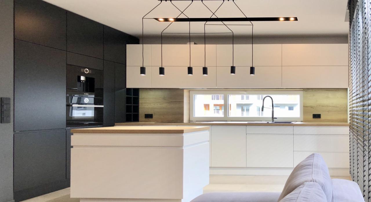 Nowoczesna kuchnia z czarnymi szafkami, białymi frontami i wyspą z drewnianym blatem oraz designerskim oświetleniem sufitowym.