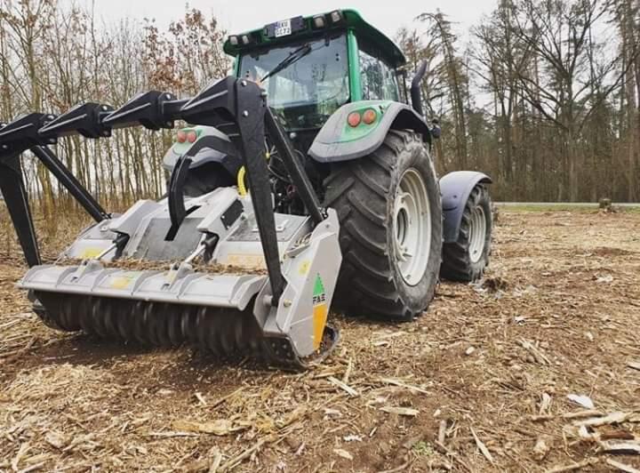 Zielony traktor z frezarką do pni drzew na polu po wycince, widoczne ścięte pnie drzew w tle.