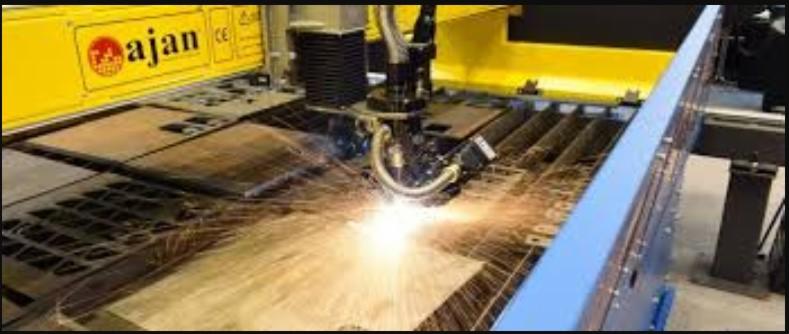 Proces cięcia metalu na maszynie CNC z widocznymi iskrami i logo producenta 'ajan' na żółtej obudowie.